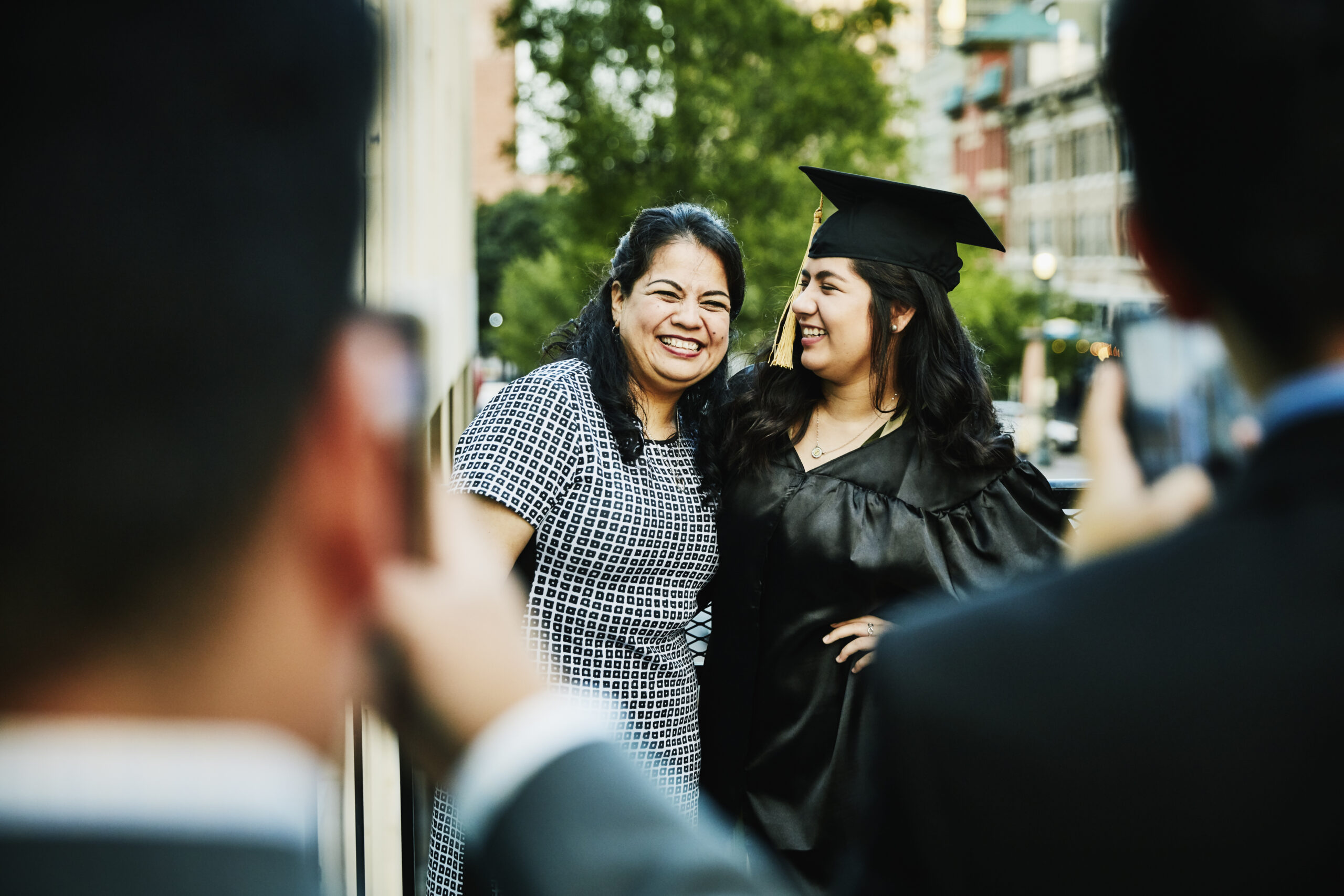 Laughing mother and daughter posing for graduation photos during dinner on restaurant deck
