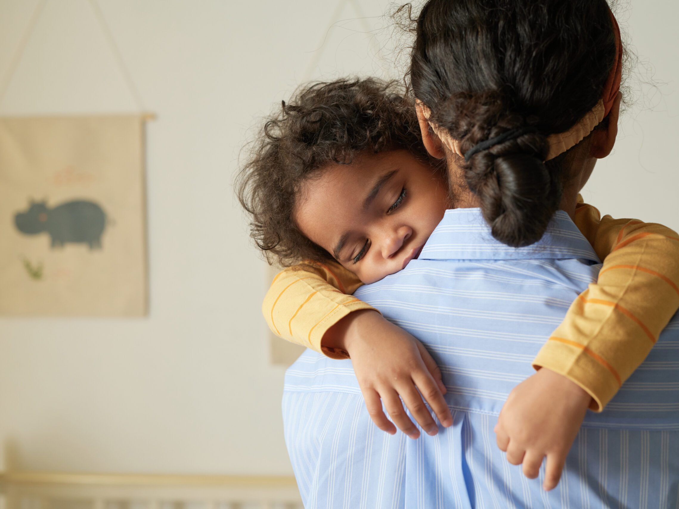 Back view of African American teenage girl holding sleeping little sister in arms while babysitting, copy space