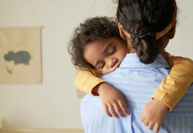 Back view of African American teenage girl holding sleeping little sister in arms while babysitting, copy space
