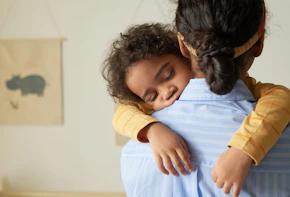 Back view of African American teenage girl holding sleeping little sister in arms while babysitting, copy space