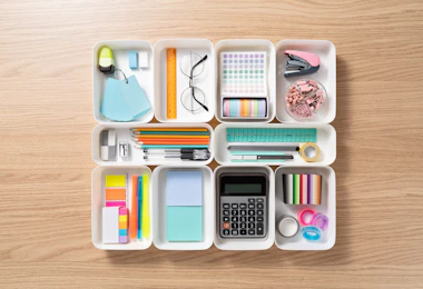 Neatly Organized Stationery in White Trays on Beige Colored Wood Desk Directly Above View.